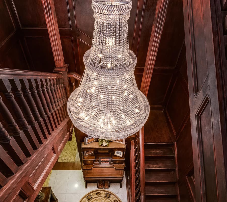 A stylish chandelier hangs over a wooden staircase in an elegantly designed foyer.