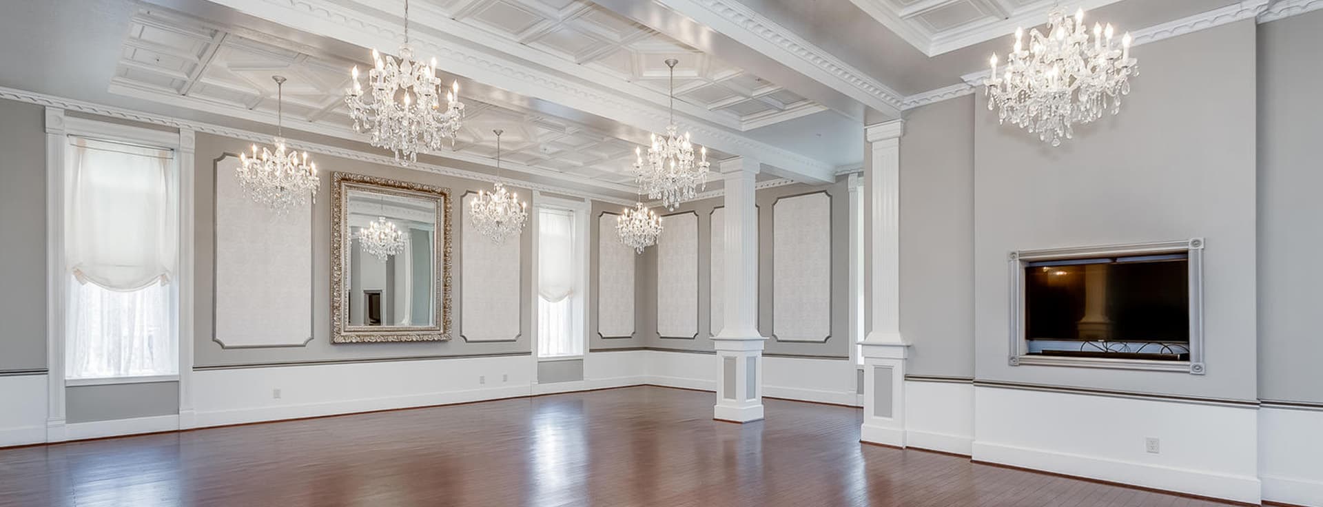 Elegant room with chandeliers, ornate molding, and large windows.