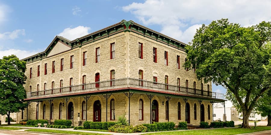 Historic stone building with red accents and a covered porch, surrounded by greenery.