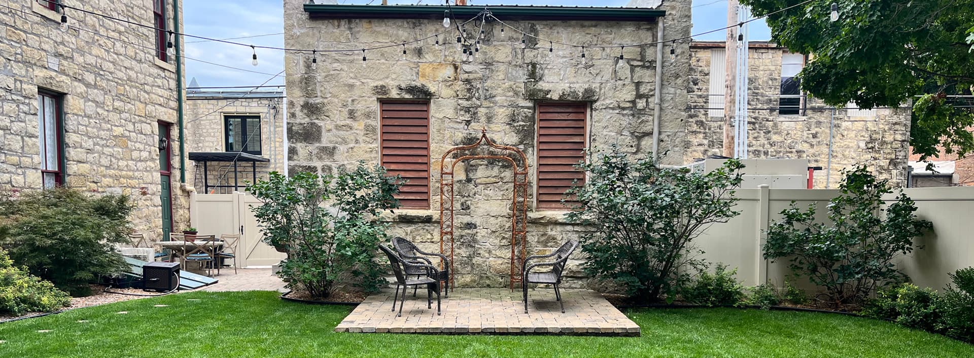 A quaint outdoor space featuring stone walls, two chairs, and lush greenery.