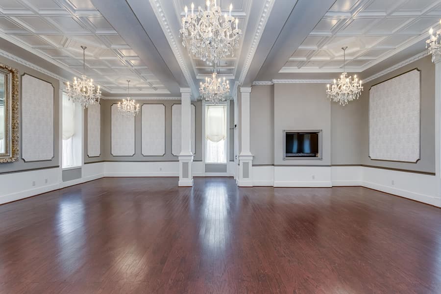 Spacious, elegantly designed room with wooden floors, chandeliers, and a modern centerpiece television.