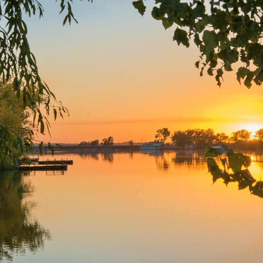 A tranquil sunset over a calm lake, framed by leaves.