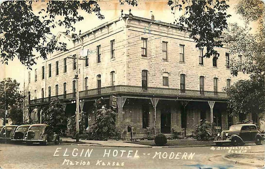 Historic postcard of the Elgin Hotel in Marion, Kansas, featuring its stone facade and vintage cars parked outside.