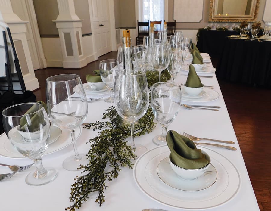 A elegantly set dining table with green napkins and glassware, accented by greenery.
