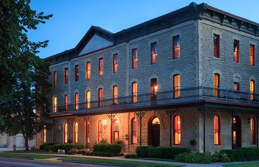 Historic stone building with illuminated windows, set against a twilight sky.