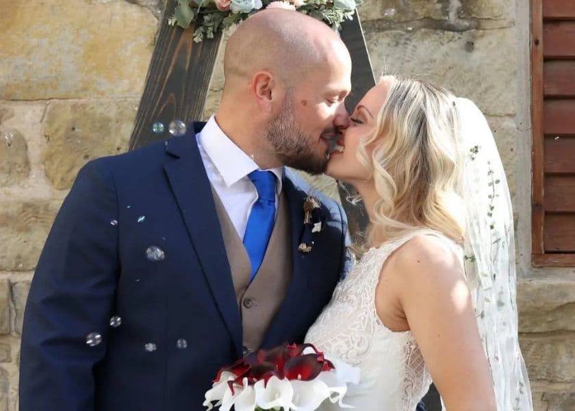 A bridal couple kissing outside under a floral arch after their elopement ceremony, while bubbles float around them. A bridal couple kissing outside under a floral arch after their elopement ceremony, while bubbles float around them.
