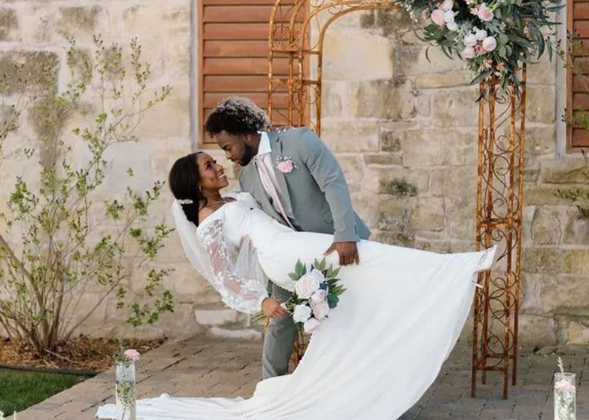 a groom dipping a smiling bride near an arch at the historic elgin hotel while she holds white roses a groom dipping a smiling bride near an arch at the historic elgin hotel while she holds white roses