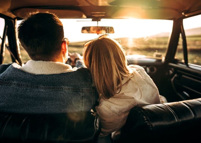 A couple embraces in a vintage car, with the sun setting in the background. A couple embraces in a vintage car, with the sun setting in the background.