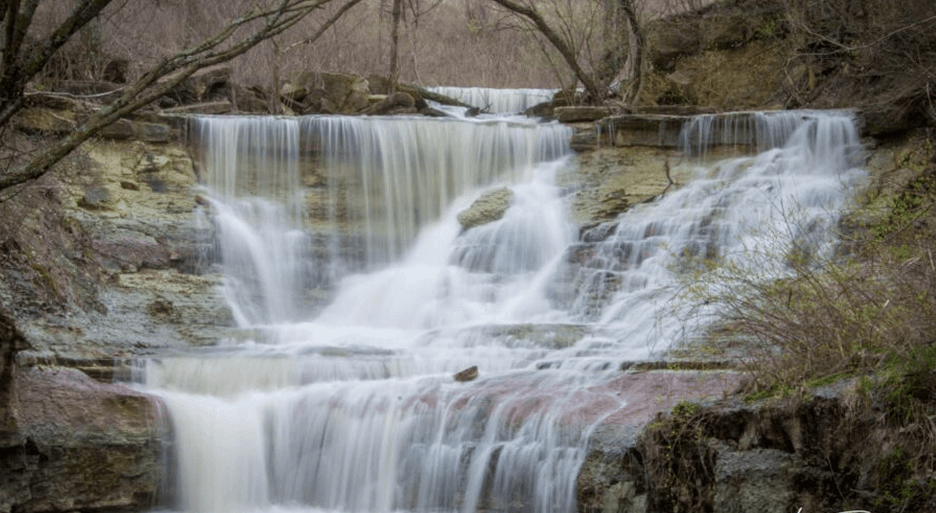 Water cascades down rocky layers in a serene waterfall surrounded by trees.