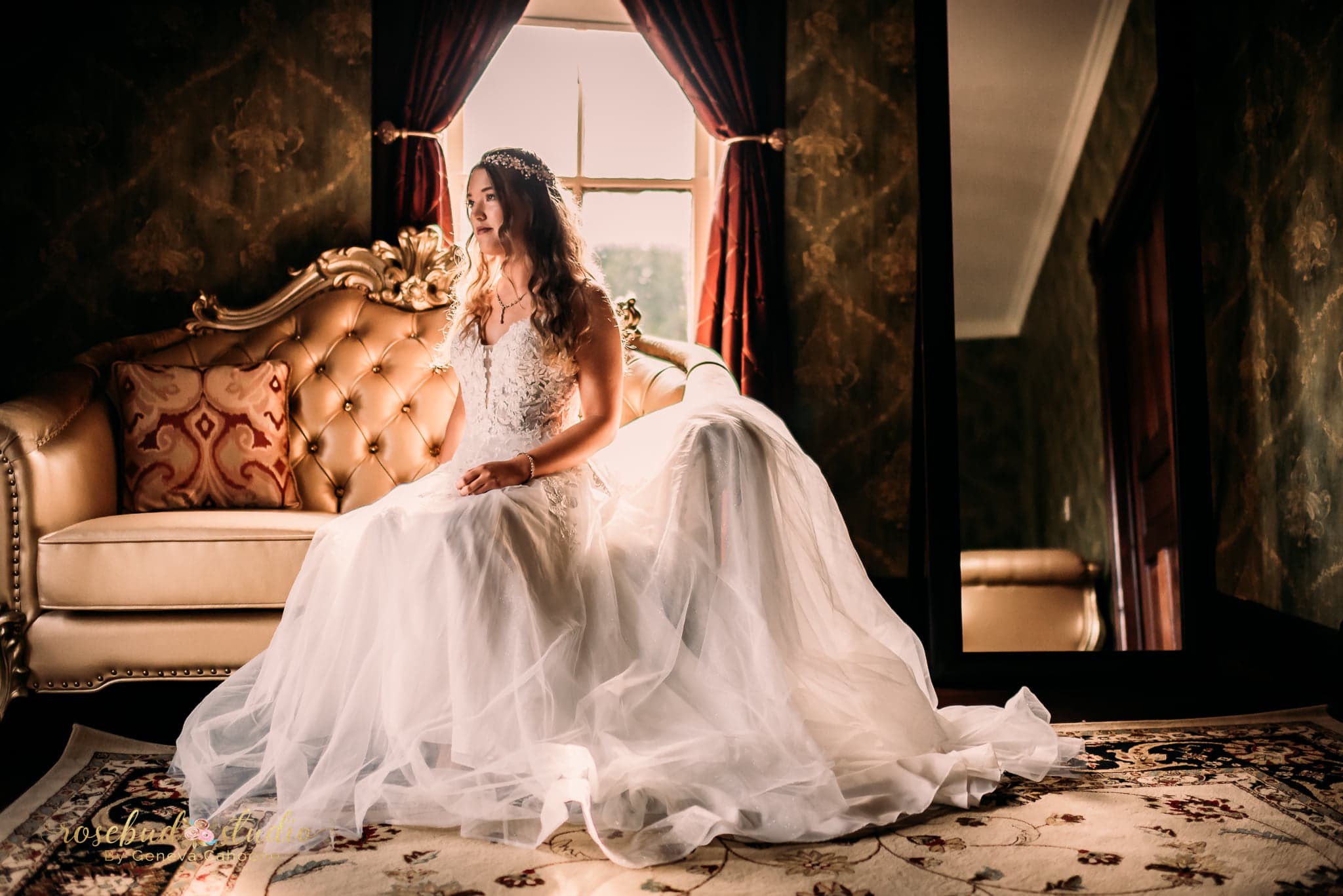 A bride in a flowing white dress sits on an elegant sofa by a window, reflecting on her special day.