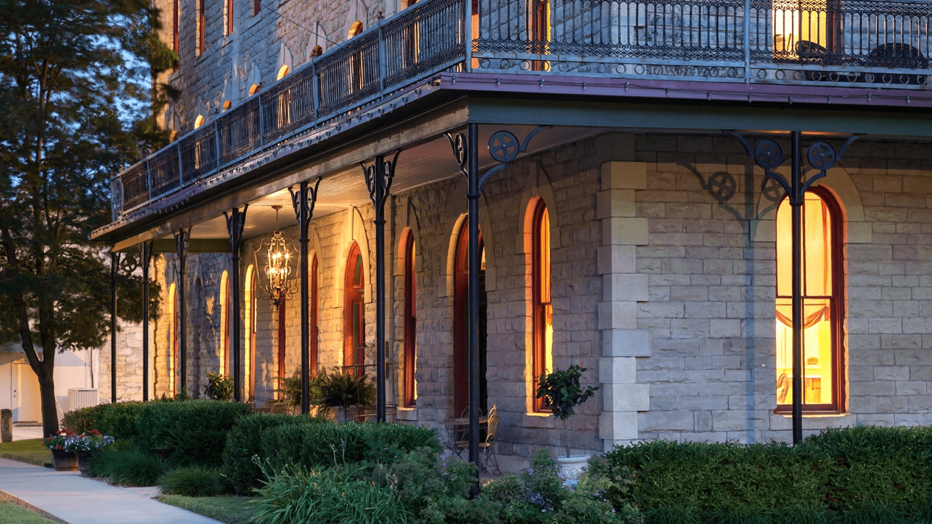 Exterior view of the Historic Elgin Hotel in Marion, Kansas, showcasing the restored 19th-century limestone architecture, wraparound porch, and glowing windows at dusk.