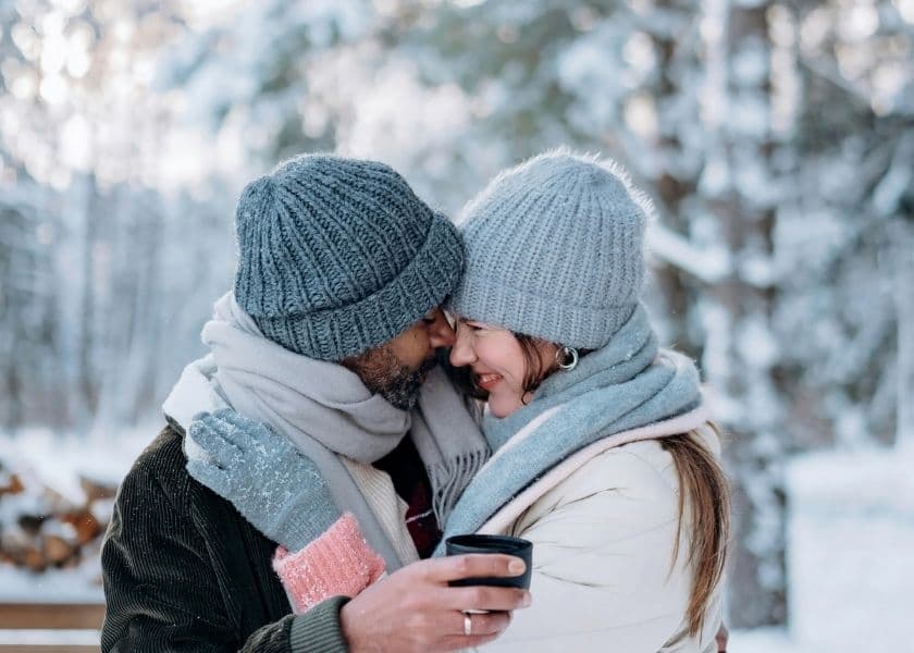a man and smiling woman outside in winter hugging while the man holds a thermos cap a man and smiling woman outside in winter hugging while the man holds a thermos cap