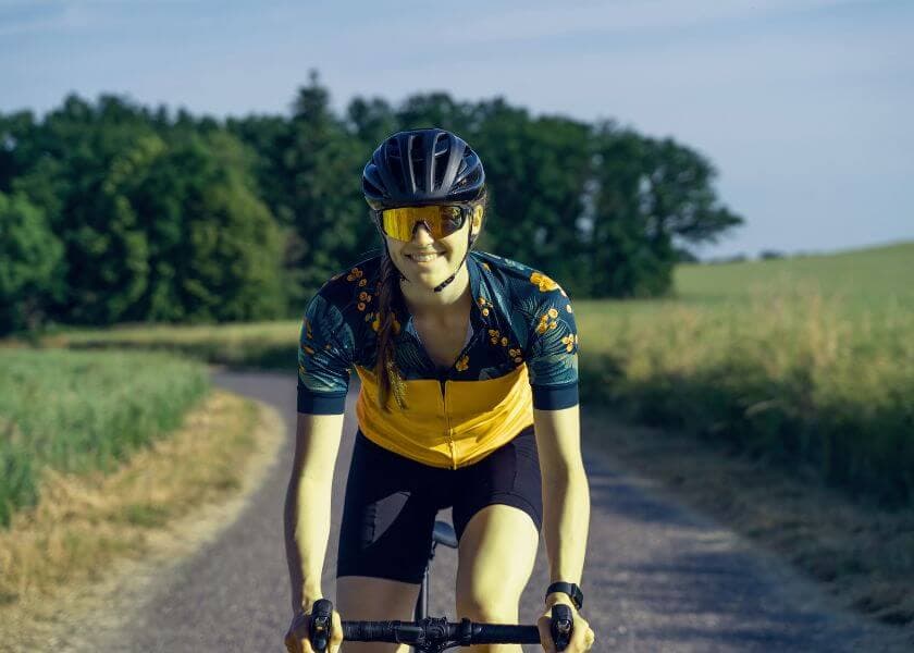a woman wearing a helmet, sunglasses, and athletic apparel while riding a gravel bike on a trail. a woman wearing a helmet, sunglasses, and athletic apparel while riding a gravel bike on a trail.